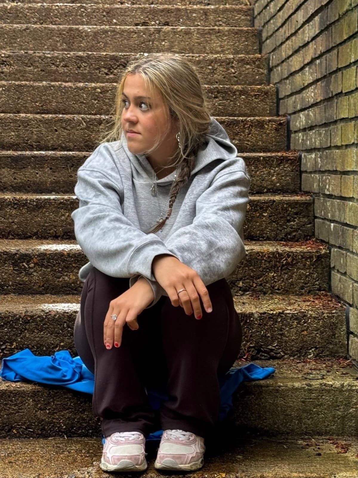Daisy sitting on stone steps in a grey hoodie